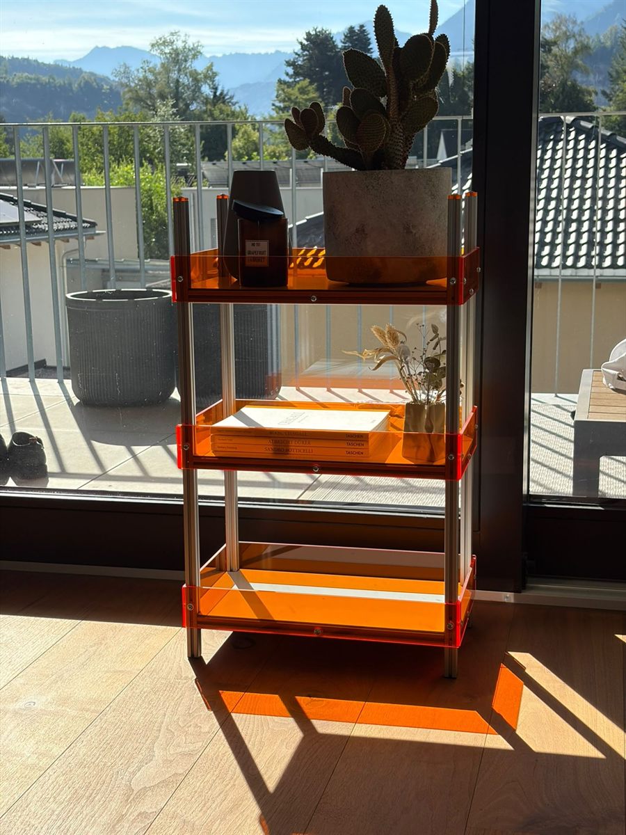 Regal mit orangefarbenen Ablagen vor einer Fensterfront mit Bergblick
